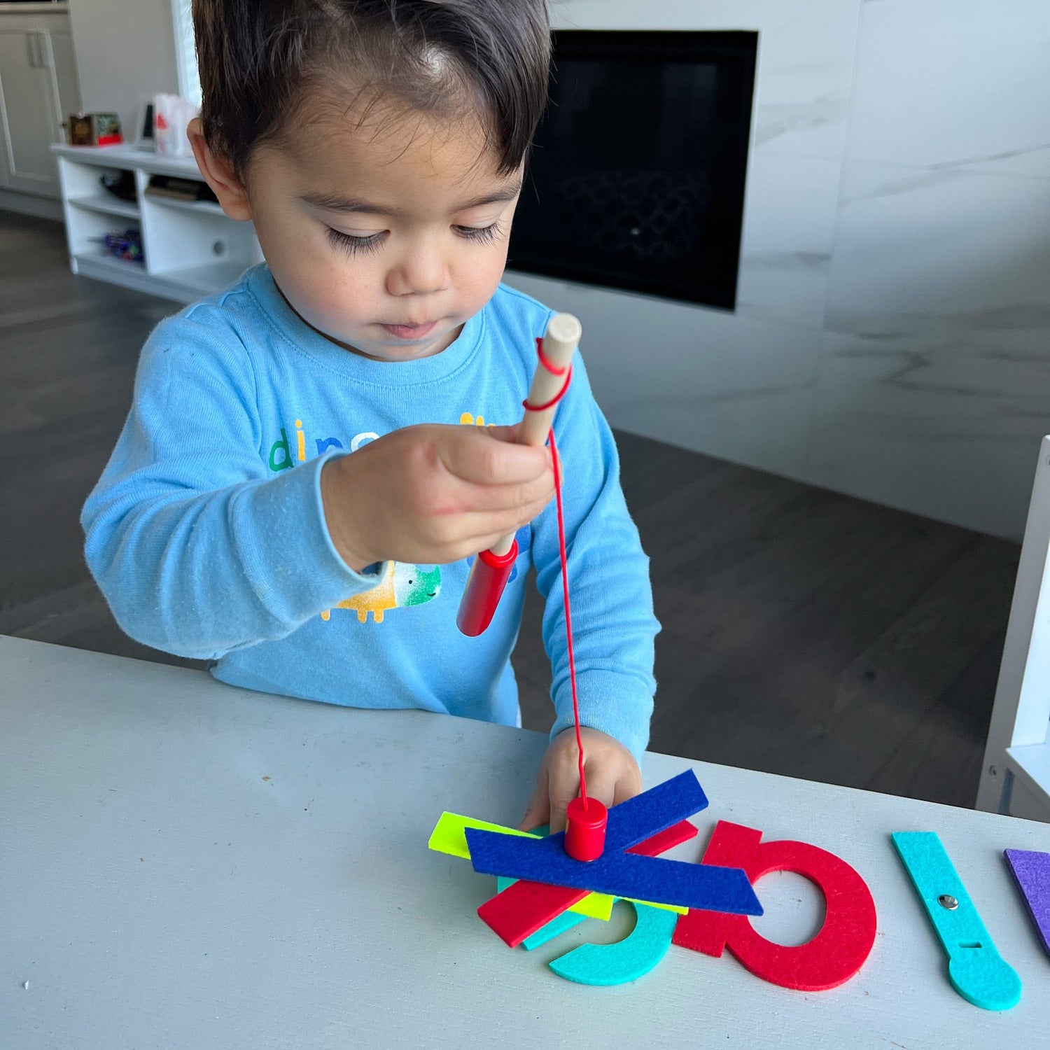 Child playing with colorful magnetic letters on a table in a modern living room.