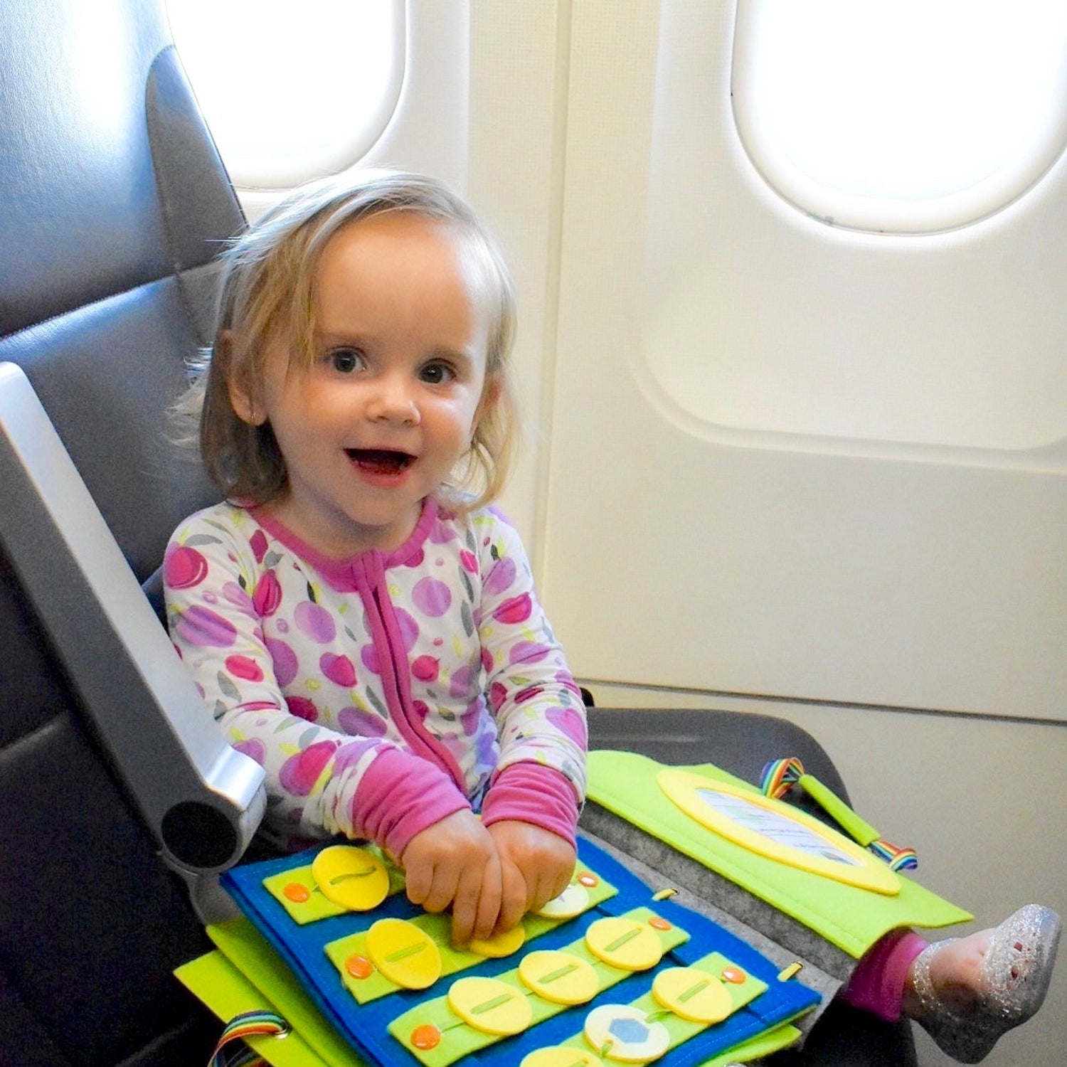 Child sitting on an airplane seat with a colorful activity book