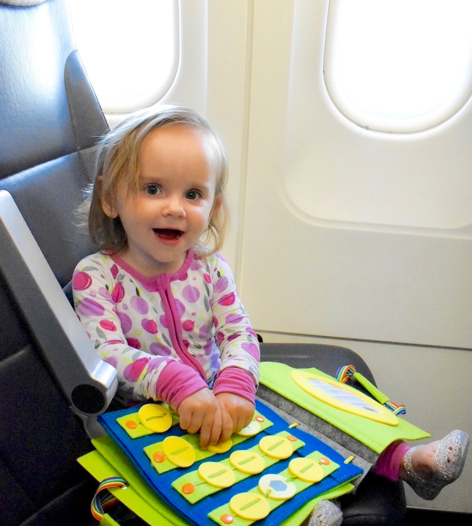 Child sitting on an airplane seat with a colorful activity book