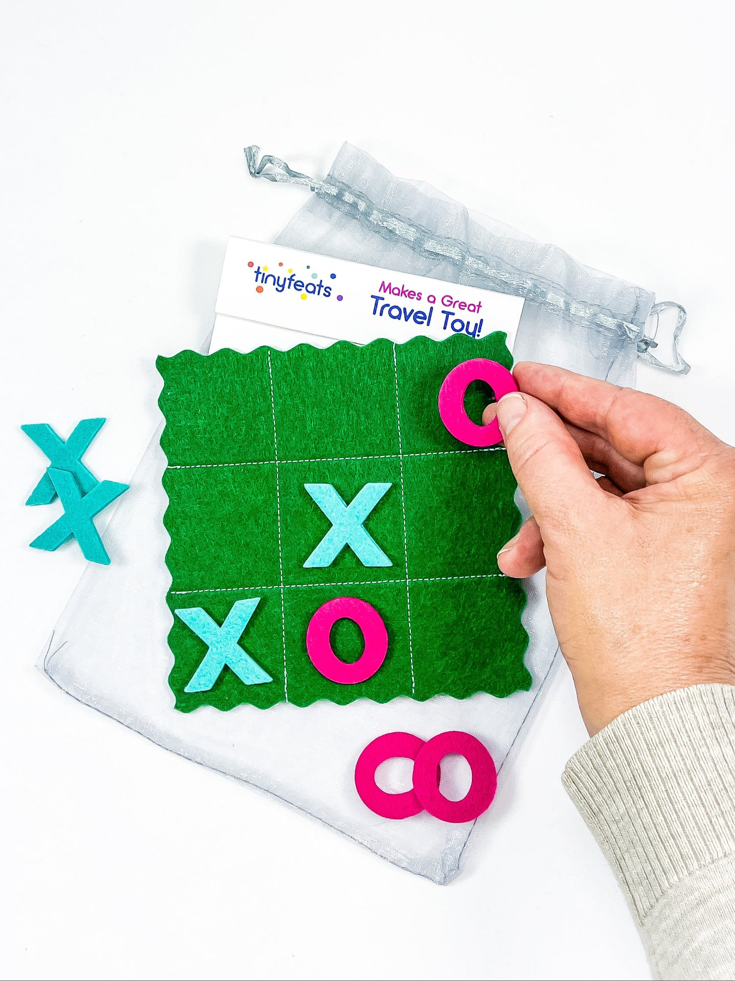 Hand holding a travel-sized tic-tac-toe game with markers on a white background