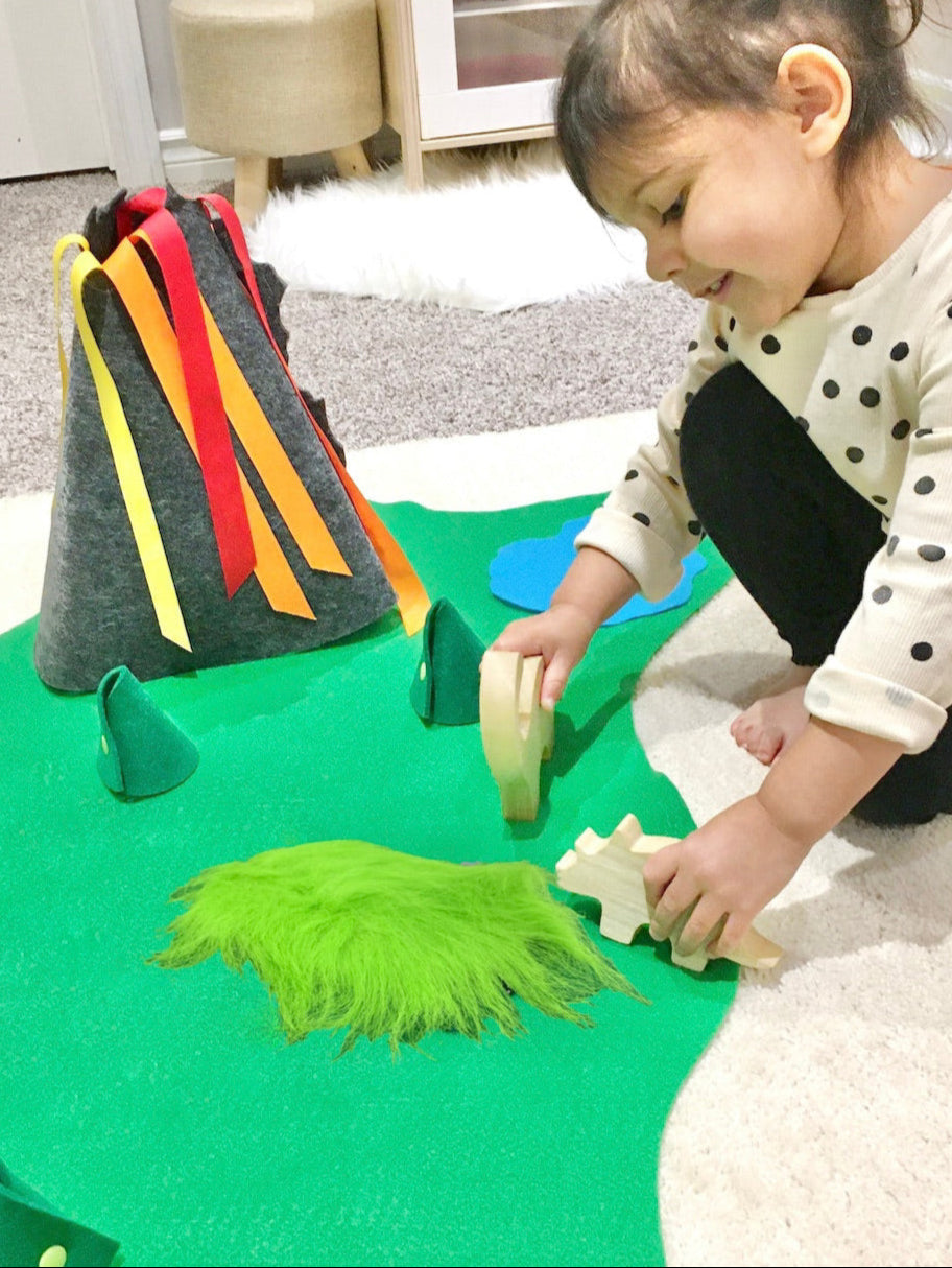 Child playing with wooden dinosaur toys with a felt volcano